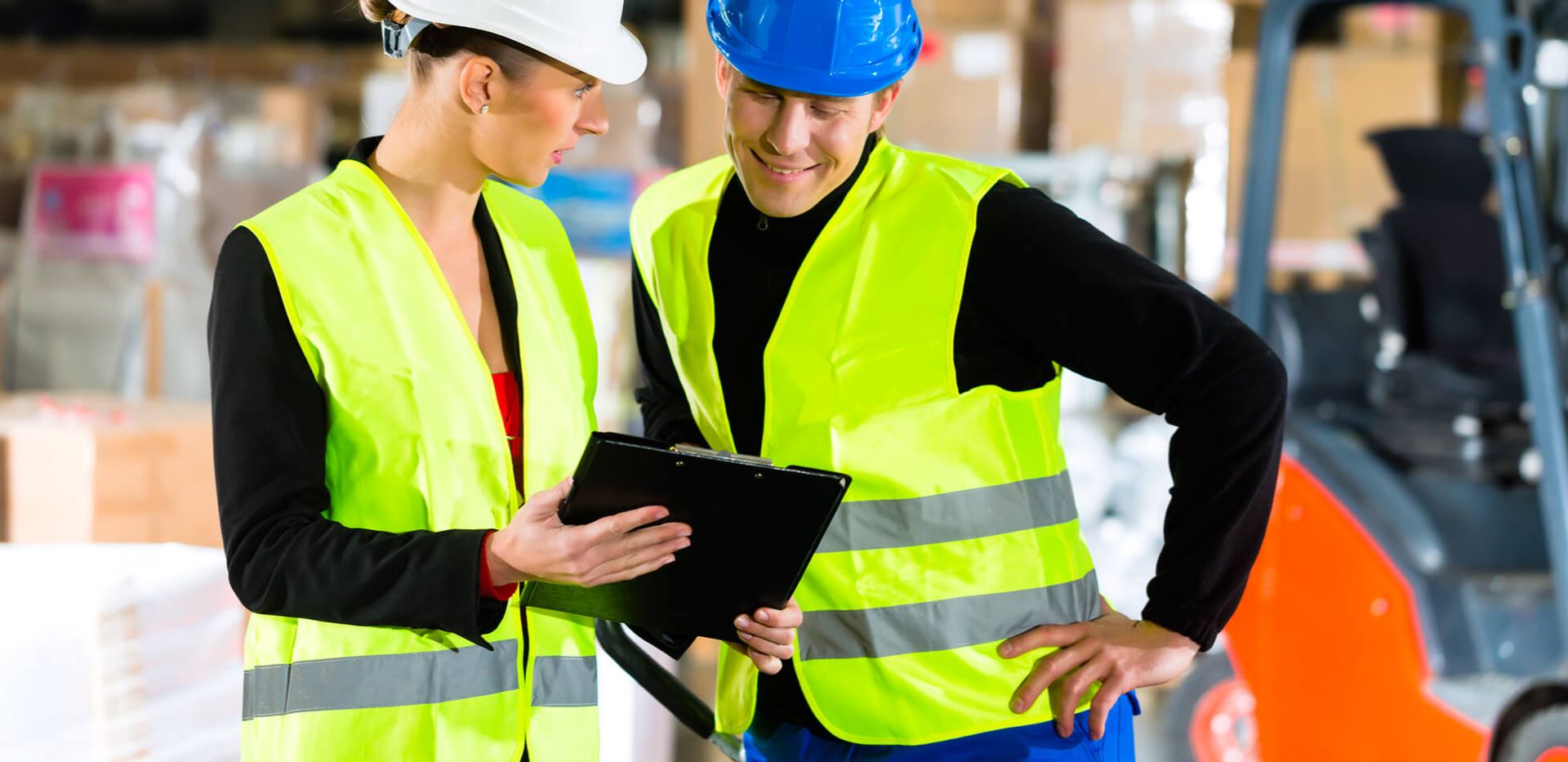Zwei Mitarbeiter schauen gemeinsam in Sicherheitskleidung auf ein Klemmbrett